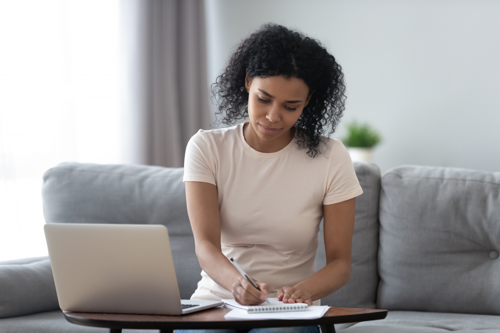 A woman writing on a legal pad with her laptop nearby